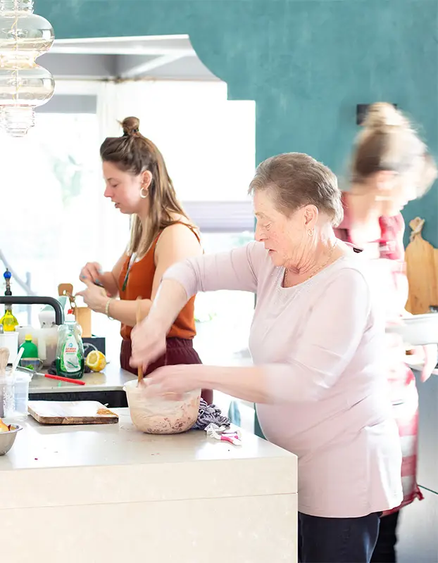 Ingrid en Anouk staan in een lichte keuken aan een werkeiland te koken voor de fotografie van hun kookboek