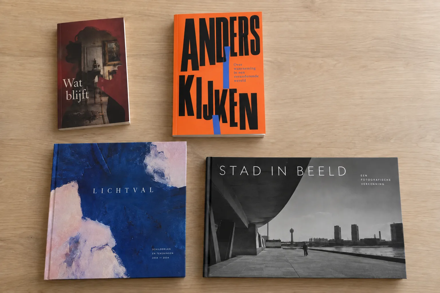 Vier boeken met verschillende staande, vierkante en liggende formaten liggen naast elkaar.